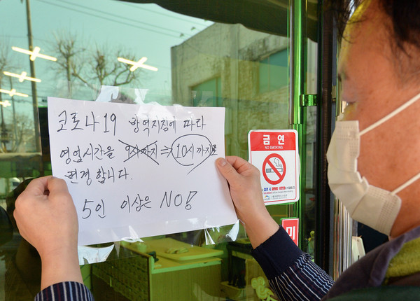 ▲ 한 식당 주인이 변경된 영업시간을 알리는 안내문을 붙이고 있다. /뉴시스