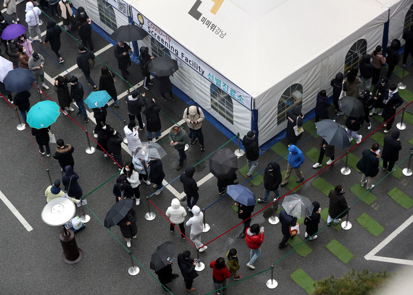 ▲ 서울 강남구보건소 선별진료소에서 우산을 쓴 시민들이 코로나19 검사를 받기 위해 길게 줄 서 있다. /뉴시스