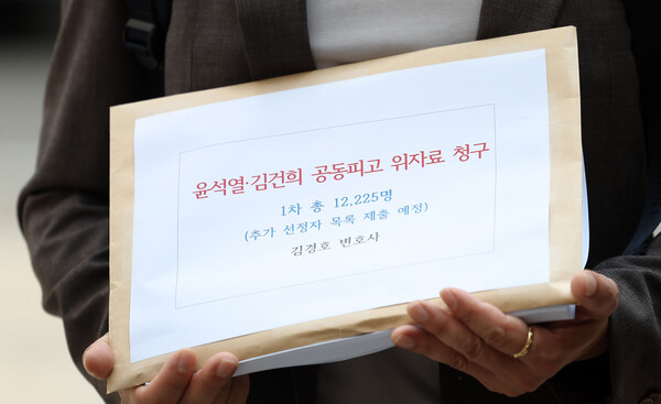 ▲ 김경호 변호사가 18일 서울 서초구 서울중앙지법에서 전직 대통령 윤석열과 부인 김건희를 상대로 1인당 10만원의 위자료(소송 신청인 1만2225명)를 청구하는 '불법 계엄 위자료' 손해배상 소송 소장 접수를 앞두고 입장을 말하는 옆에서 관계자가 청구 소장을 들고 있다. /뉴시스